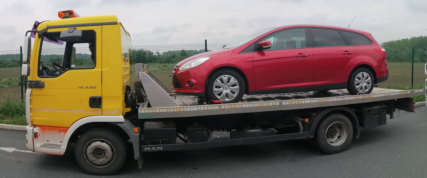 Ein roter Kombi auf dem Plateau eines gelben Abschleppwagens, auf einem Rastplatz an der Autobahn.