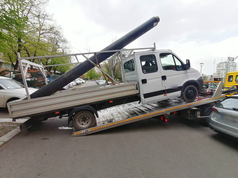 Ein Doppelkabiner mit einem langen Rohr auf der Ladefläche fährt auf das gekippte Plateau eines Abschleppwagens.