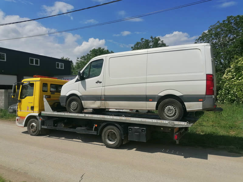 Ein weißer Volkswagen Crafter auf dem Plateau eines gelben Abschleppwagens, von der Seite.