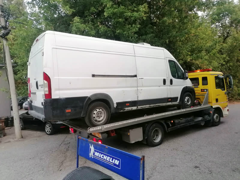 Ein weißer Fiat Ducato mit Hochdach auf dem Plateau eines gelben Abschleppwagens, von hinten gesehen.