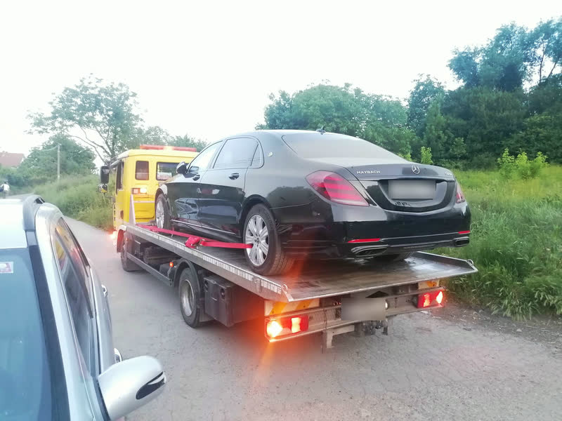 Ein schwarzer gepanzerter Mercedes-Maybach, mit roten Gurten auf dem Plateau eines gelben Abschleppwagens gesichert, von hinten gesehen, in der Dämmerung.