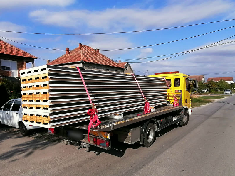Ein Stapel Sandwichpaneele, mit roten Gurten auf dem Plateau eines Abschleppwagens gesichert, in einer Wohnstraße.